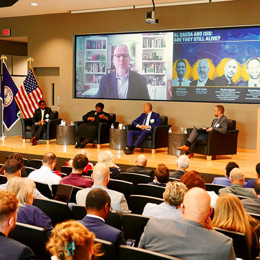 Four people sitting in chairs on a stage have a discussion while an audience listens